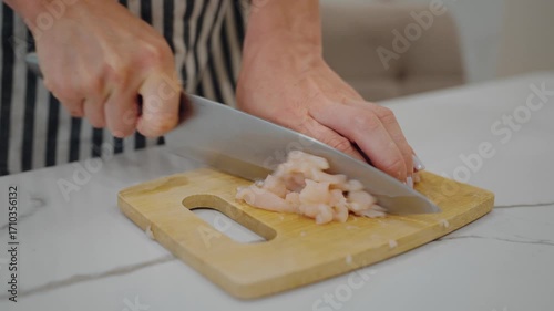 Mother cooking dinner for children, cutting chicken fillet, fresh organic food. Closeup view of female hands with knife and chopping board on home kitchen table, nutrition for health and slenderness