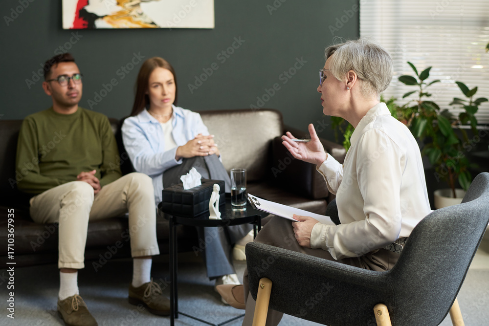 Obraz premium Middle aged woman psychologist conducting therapy session with man and woman sitting on couch listening attentively