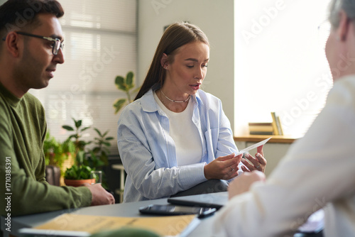 Woman holding paper while sitting with man and South Asian man, discussing psychological assessment in office setting