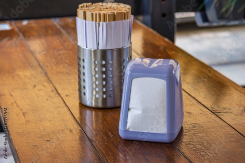 Foto Metal holder with wooden chopsticks and plastic napkin dispenser on wooden table