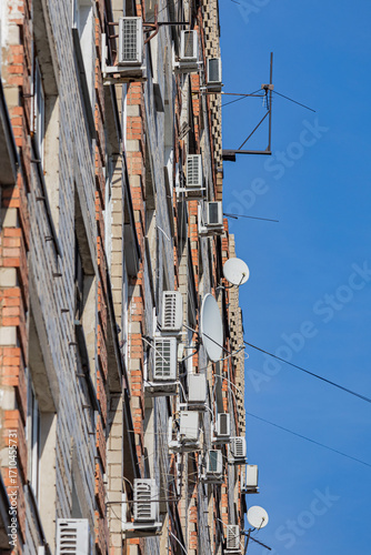The wall of a multi-storey apartment building with numerous air conditioners and antennas. Soft focus