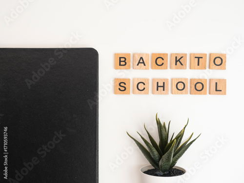 Back to school written in wooden blocks on a white background. The blocks are arranged in such a way as to form the words Back to School between the book objects and flowers as decoration.
