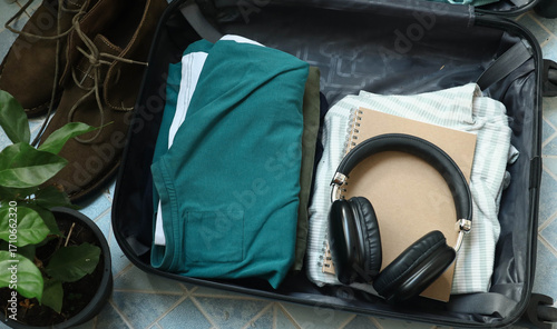 Close up of a person getting ready for travel and packing clothes into an open black suitcase, vacation travel concept. Person preparing for a trip and folding clothes into an open luggage.