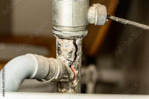 Broken drain pipe under bathroom sink, leaking water. Plumbing problem, home maintenance or emergency repair situation. Concept for household damage, insurance, plumbing services