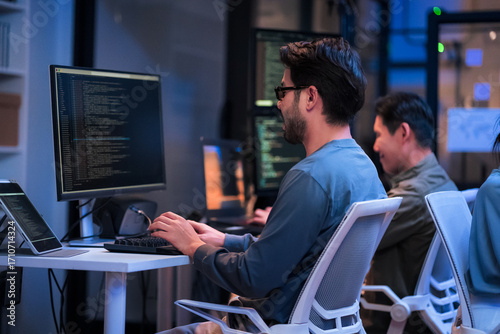 young Asian software development manager leads a late-night office discussion with his executive team, mentoring developers and analyzing source code to guide programming and project development