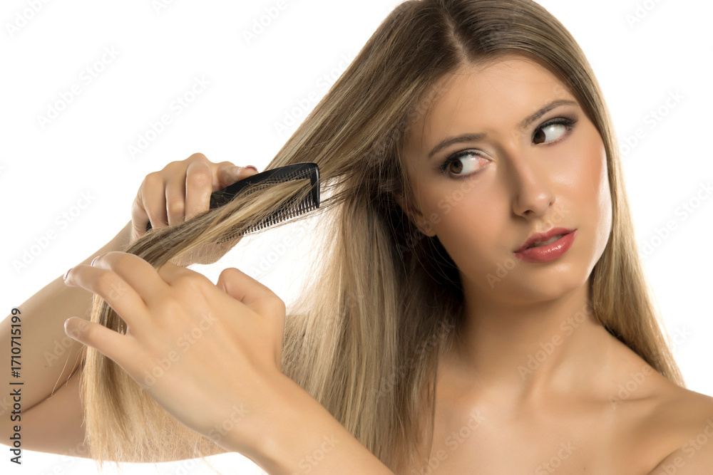 Fototapeta premium Studio shot of young blonde woman combing long straight hair with black comb on white background.