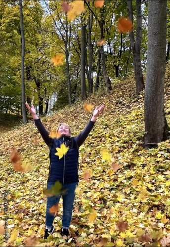 A woman aged 40-50 is throwing up autumn leaves in nature.
