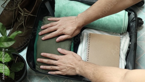 Close up of an unrecognized person getting ready for travel and packing clothes into an open black suitcase, vacation travel concept. Person preparing for a trip and folding clothes into a luggage