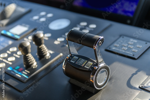 A close-up view of a yacht or ship bridge with the throttle controls. The navigation radar screen and electronic control panels are visible in the background