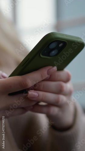 Close-up of woman holding iPhone and operating it, with soft focus on phone and hands, glass window visible in background, focus on mobile device interaction in modern setting