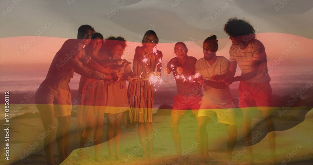 Fototapeta premium Eight friends leaning on sandy beach at sunset over ocean horizon, with handheld sparklers glowing
