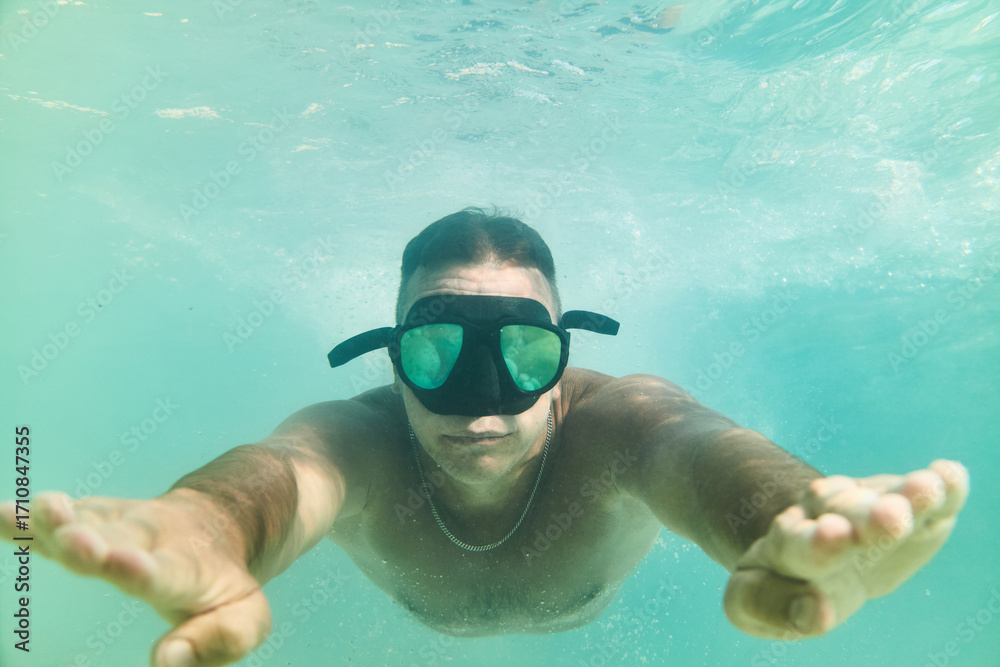 Naklejka premium Man enjoys swimming underwater in clear blue water wearing a mask and fins during sunny daytime activity