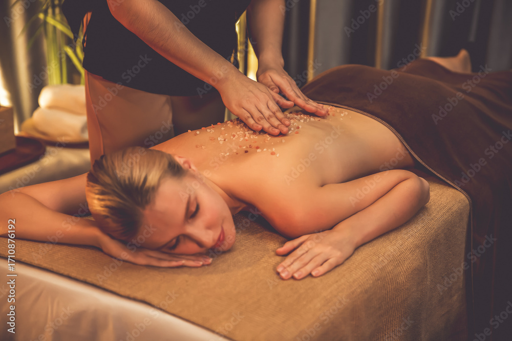 Obraz premium Woman customer having exfoliation treatment in luxury spa salon with warmth candle light ambient. Salt scrub beauty treatment in Health spa body scrub. Quiescent