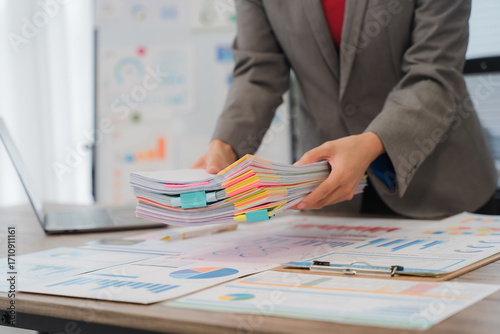 Businesswoman browsing through various documents, efficiently organizing files and managing paperwork in a bustling office environment, tackling deadlines and ensuring smooth operations