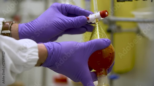 Close-up detailed view of a woman shaking a pear-shaped filtering flask, testing its tap, and attaching it to lab apparatus — perfect for themes of science, chemistry, precision, and laboratory work.