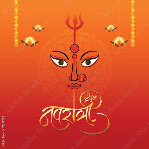 A vibrant illustration of the face of Goddess Durga with a trident and bells, celebrating the auspicious Hindu festival of Navratri against a warm orange-red background.