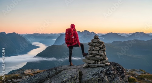 Female hiker enjoying mountain view at sunrise with rock cairn overlooking fjord