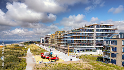 A vibrant, red play boat sits on a sandy playground near a modern residential area by the sea at Kijkduin in The Hague. The scene is bright and inviting, with families enjoying the coastal view.