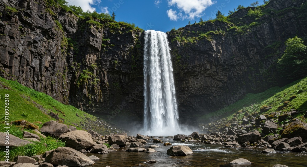 Fototapeta premium Majestic waterfall cascading down a cliff face surrounded by lush green foliage under a clear blue sky