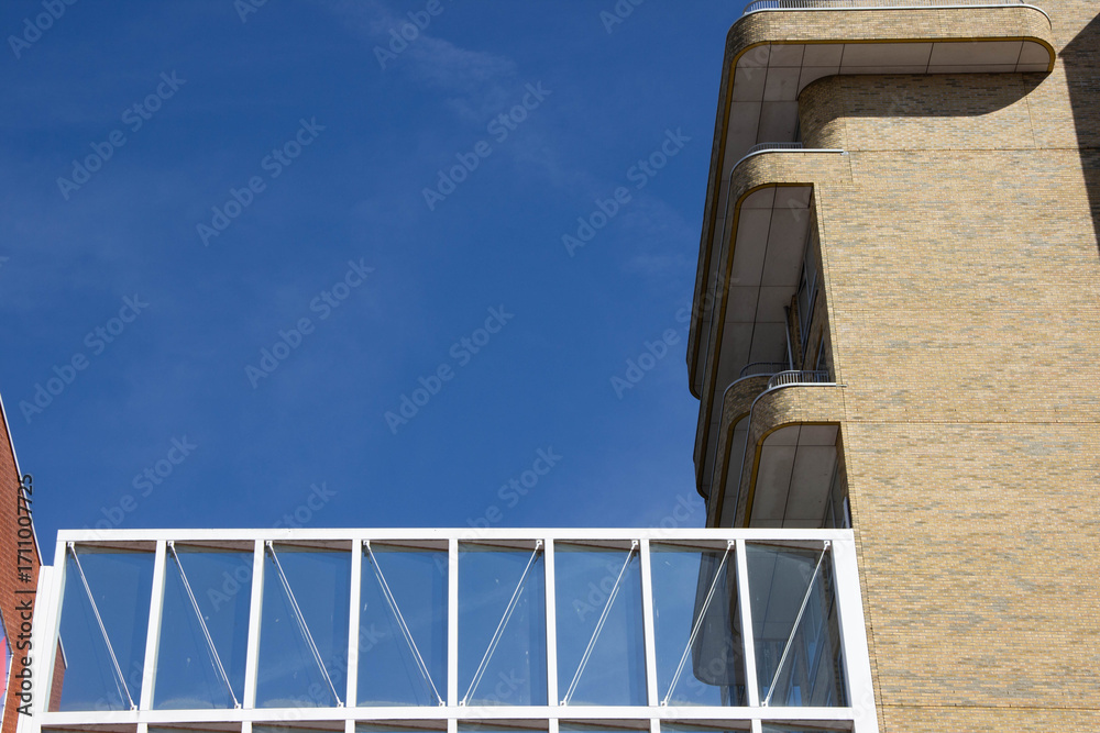 Obraz premium Modern architectural building with a glass bridge connecting two structures against a clear blue sky, showcasing contemporary design and urban aesthetics