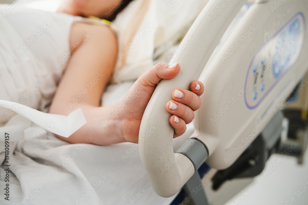 Fototapeta premium Close-up of a patient's hand holding the bed rail in a hospital room, conveying a sense of vulnerability and the need for support during medical care