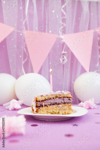 Happy birthday - purple biscuit cake with one burning candle and white and pink decorations with air balloons, vertical anniversary card