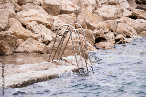 Beach ladder on breakwater rocky beach and wavy sea in tide