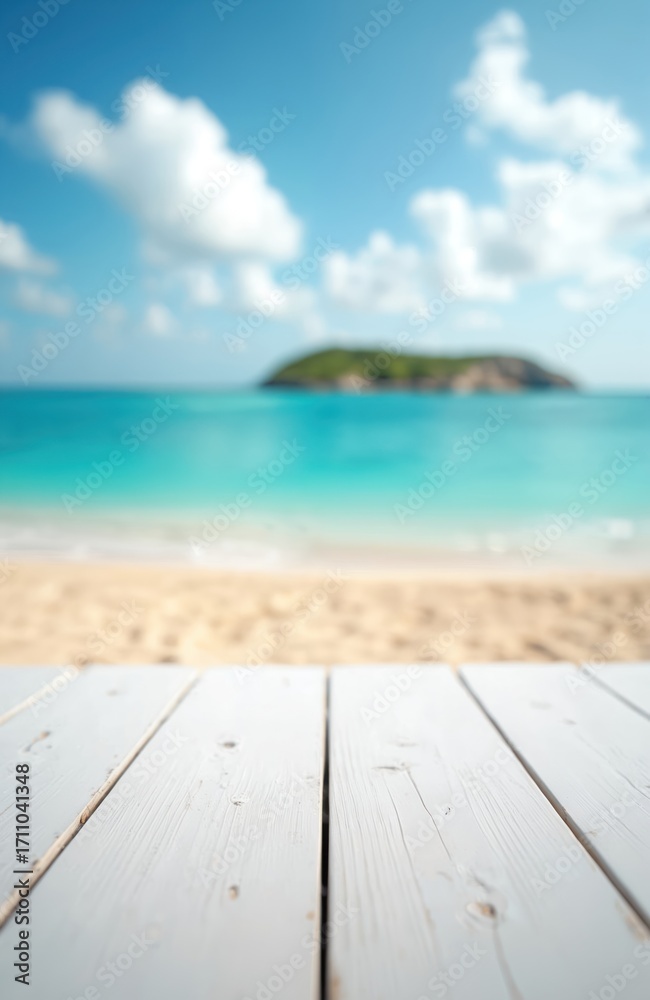 Fototapeta premium White wooden table top in foreground provides empty copy space. Blurred tropical ocean beach background with golden sand, calm turquoise water. Distant green island, clear blue sky, fluffy white