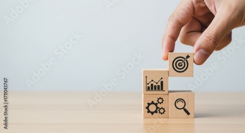 Business strategy concept with icons on wooden blocks and a hand placing the final block for success