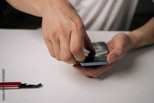 Skilled technician carefully removing damaged tempered glass screen protector from smartphone using precision repair tool, demonstrating professional device maintenance, close-up.