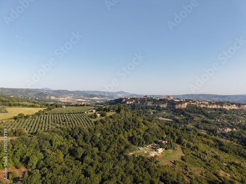 Aerial drone photo of Orvieto, a historic town in Umbria, central Italy, dramatically perched on a volcanic plateau. The view captures the hilltop town surrounded by olive groves, lush countryside.