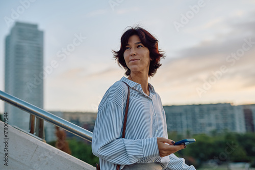 Photos Businesswoman walking confidently up stairs while holding a smartphone, gazing t
