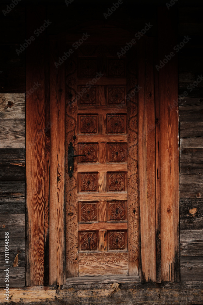 Fototapeta premium Close-up of a traditional carved wooden door in village Drvengrad, Serbia, highlighting intricate patterns and textures