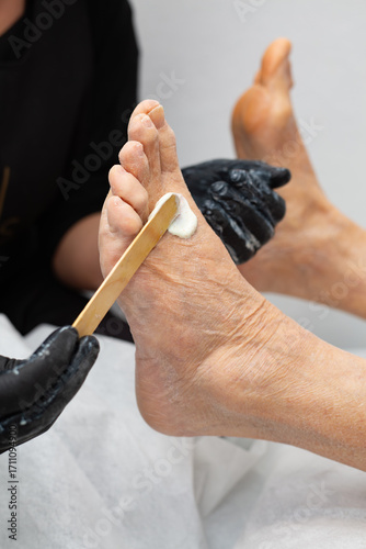 Elderly woman gets foot massage from beautician. Beautician applies scrub to feet. Rejuvenating pedicure for seniors. Self-care.