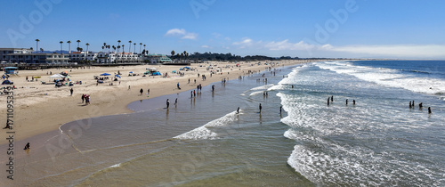 Pismo Beach as seen from a UAV Drone with the eaves and people enjoying the day as the waves hit the beach with the swells clearly seen and the city in the background