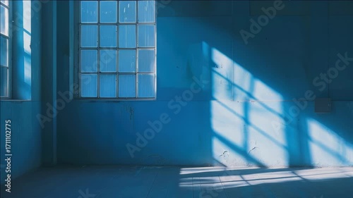An abandoned industrial space with blue walls and a concrete floor, illuminated by sparse natural light. This setting is characterized by dilapidation and monochromatic elements.