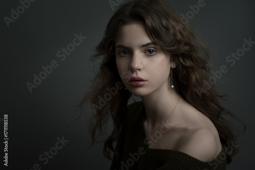 Young beautiful woman with long curly hair and young perfect skin. Model in casual clothes with perfect wavy hair. Low Key Portrait photography. Beautiful teen girl portrait.