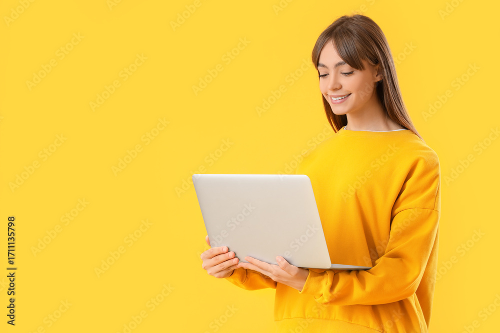 Fototapeta premium Young woman using laptop on yellow background