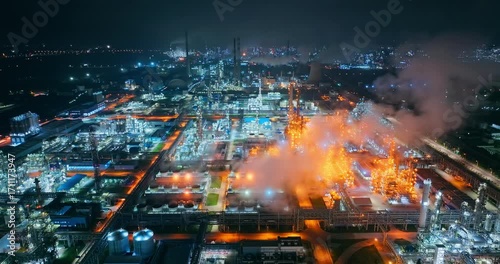 Aerial shot of a sprawling petrochemical industrial complex glowing with bright lights against the dark night sky.