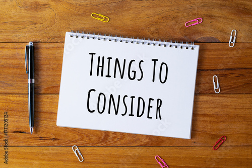 Selective focus of a pen, paper clips and notebook written with Things To Consider on wooden background.