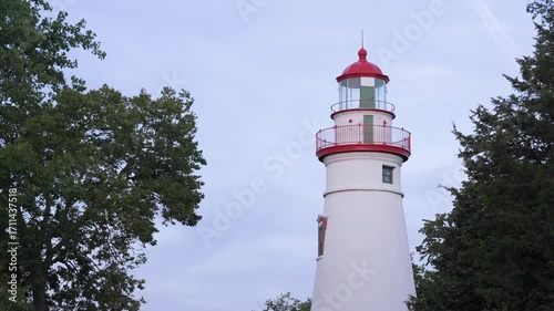 Wallpaper Mural A still midshot of the Marblehead Lighthouse in Port Clinton, Ohio, framed by trees and clear sky, highlighting its striking red and white architectural details. Torontodigital.ca