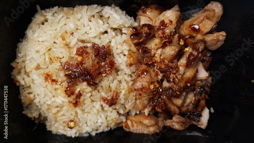 A serving of grilled chicken slices paired with steamed rice and sprinkled chili flakes, presented in a simple black container.  
