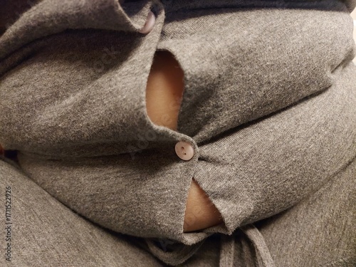 Close-up of tight grey fabric with button under pressure, symbolizing overweight, body size challenge, weight gain, unhealthy lifestyle, diet issues, and clothing not fitting properly.