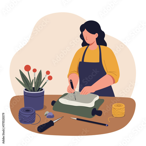 Anonymized woman in apron carefully shapes clay on table with plant and craft supplies around