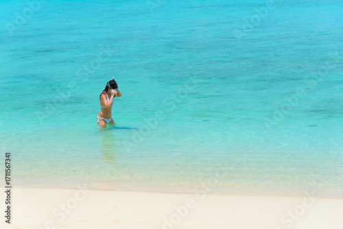 A female tourist in white bikini is enjoying beach holiday, putting on a snorkeling mask and getting ready to snorkel in the bright blue water under the sun, copy space, Koh kradan, Trang, Thailand.