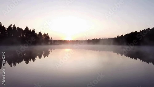 Serene lake at sunrise, mist rising over calm water surrounded by a dark forest.
