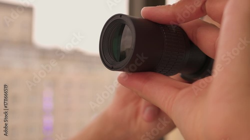 A man is intently observing the world outside his window with binoculars, showing curiosity