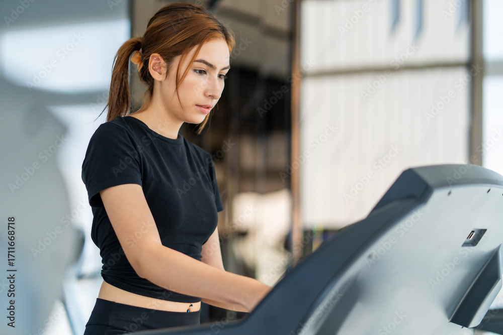 Obraz premium Young woman engages in exercise on treadmill in modern gym environment, showcasing her dedication to fitness and health. equipment around her enhances workout experience