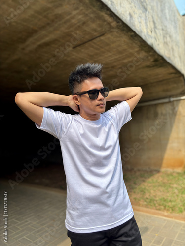Man wearing white t-shirt and sunglasses posing standing under bridge with mockup concept