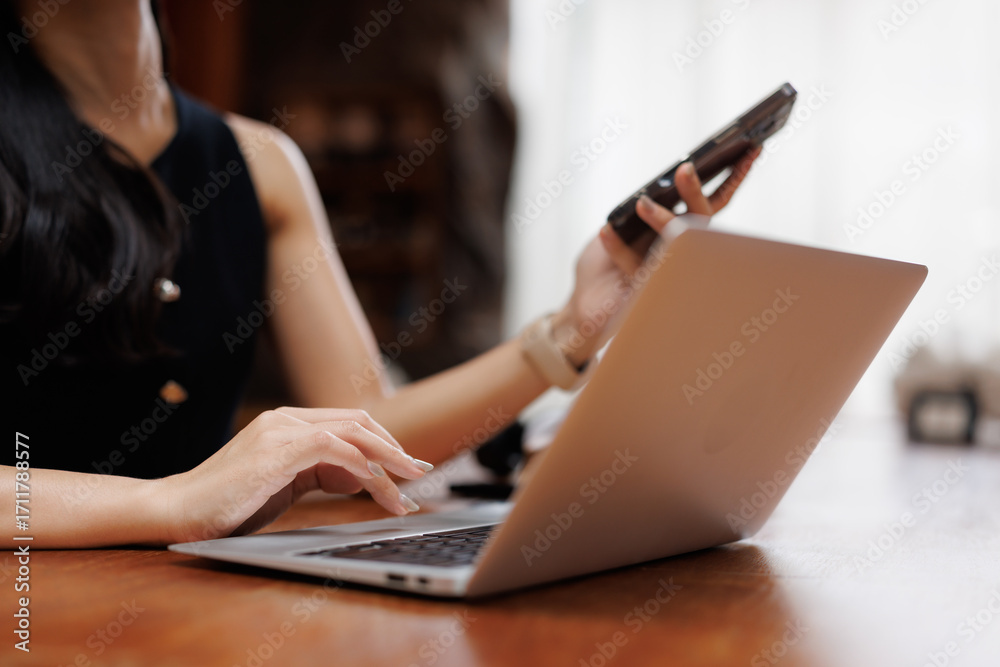 Fototapeta premium Businesswoman working on laptop and holding smartphone